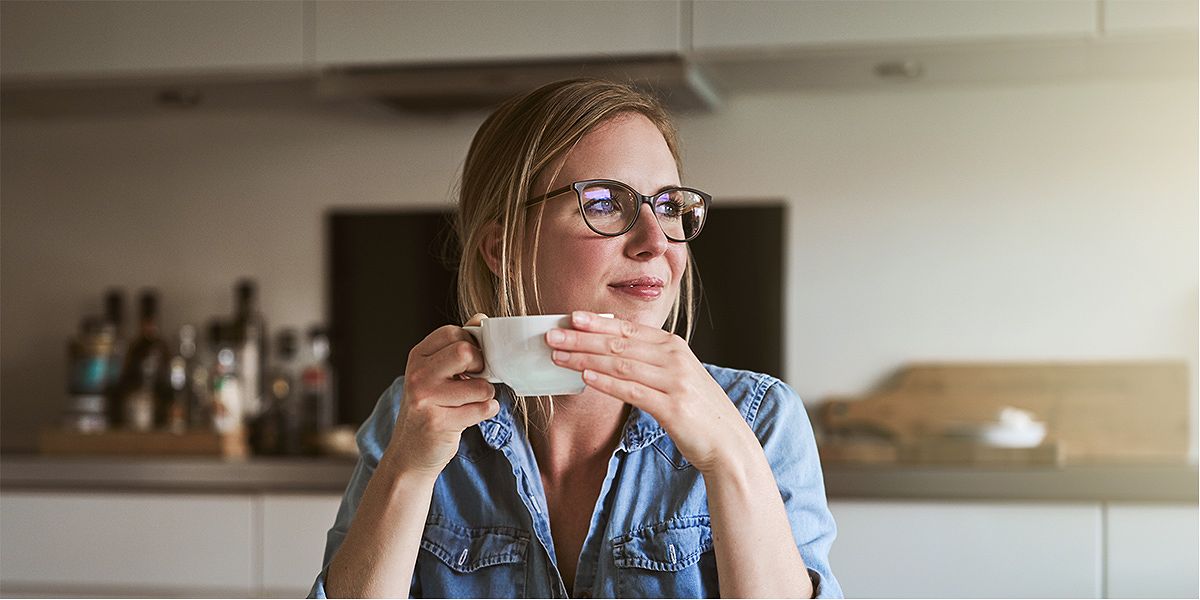 Woman holding a coffee cup looks toward her window with a relaxed expression on her face